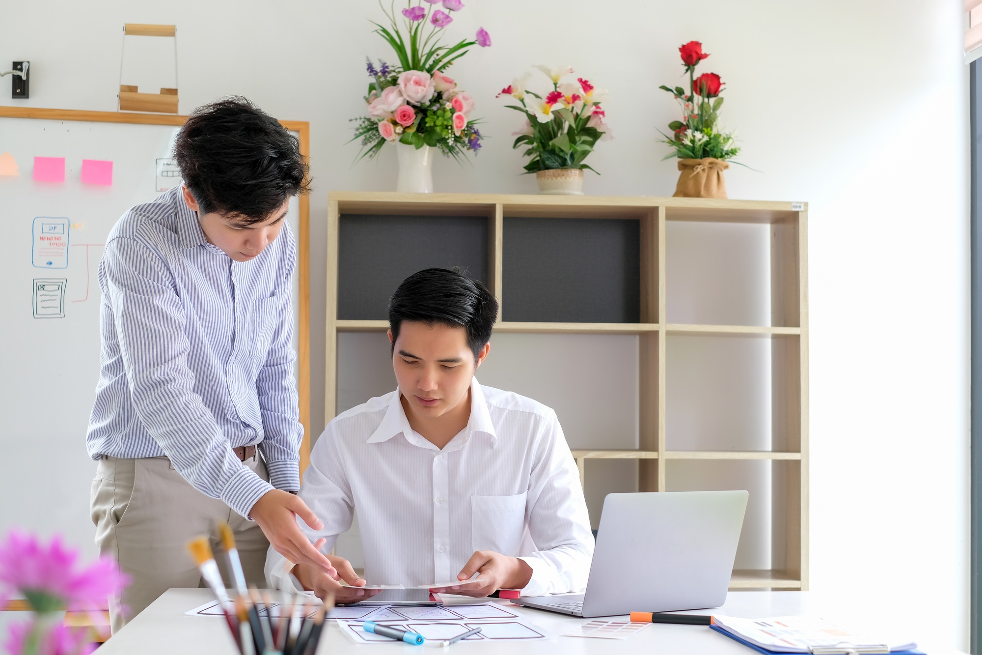 Two Asian men are working together to design websites and application on mobile phone.